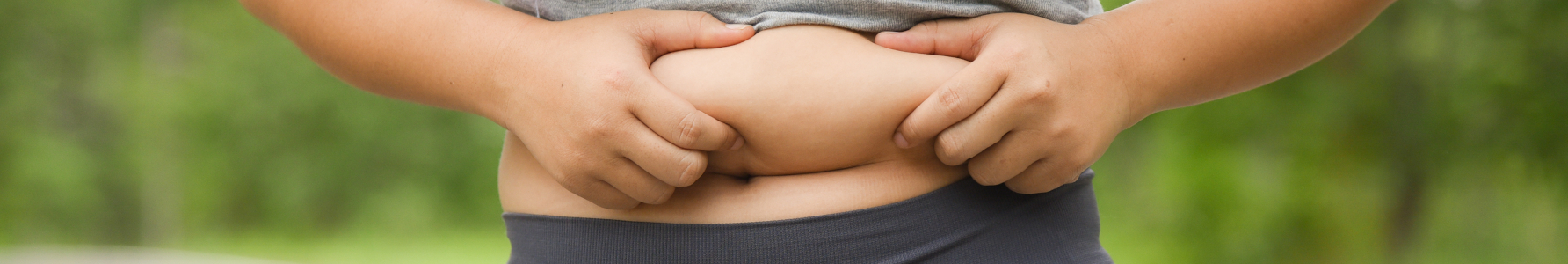 Skinny fat - kobieta w stroju sportowym trzymająca się za fałdkę tłuszczu na brzuchu